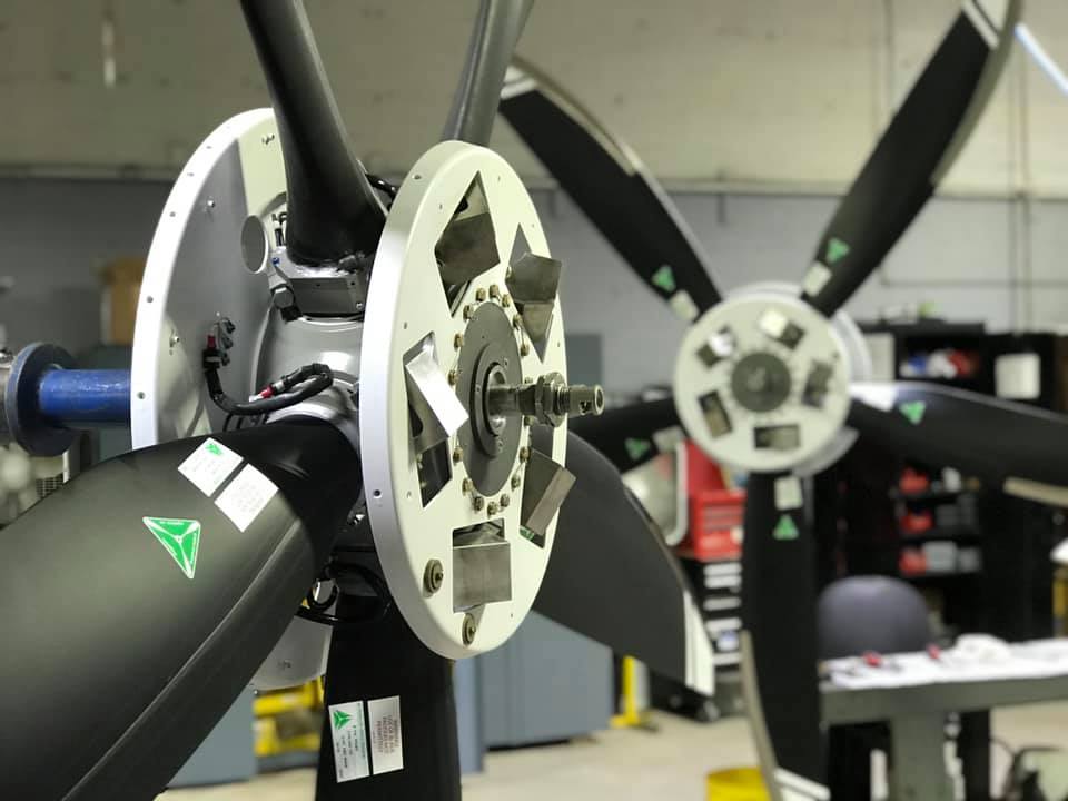 In a workshop, a worker is focused on maintaining a propeller, with tools and parts organized around the workspace.