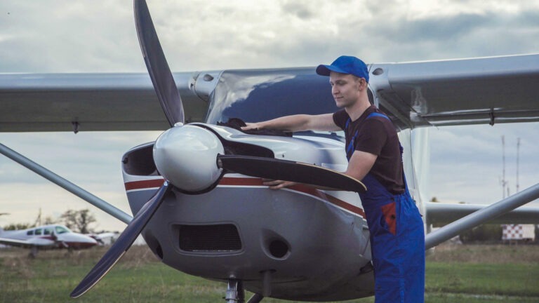 Young pilot or mechanic working on an aircraft wiping down the nose cowling on a small plane parked outdoors on an airfield